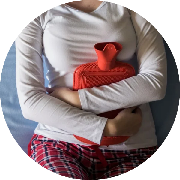 Woman holding a hot water bag near abdomen, illustrating irregular or painful menstrual cycles in PCOS.